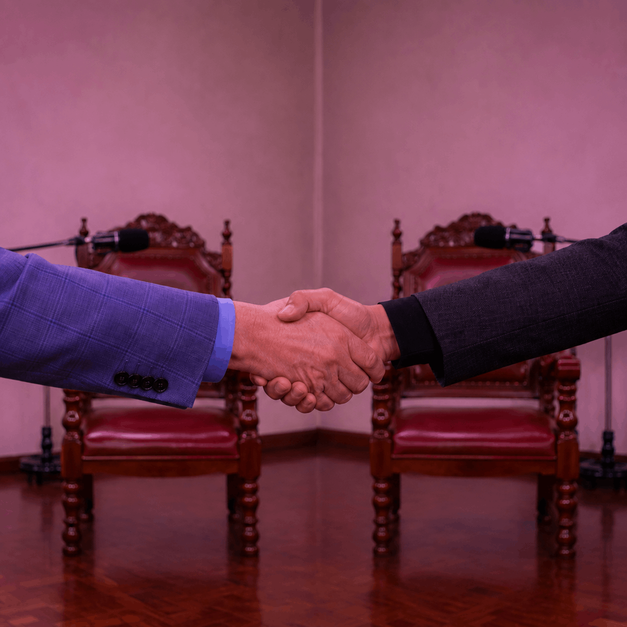 Dos personas se saludan de mano frente a dos sillas y micrófonos preparados en un estudio